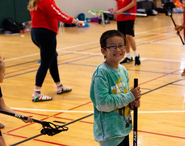Summer camp participant posing with a lacrosse stick at the YMCA