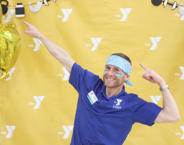 YMCA staff member poses in front of a photo backdrop for the Fitness Expo at the Morgan Family YMCA