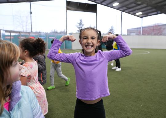 Camp participant poses by flexing during sport time in the covered playfield at the YMCA