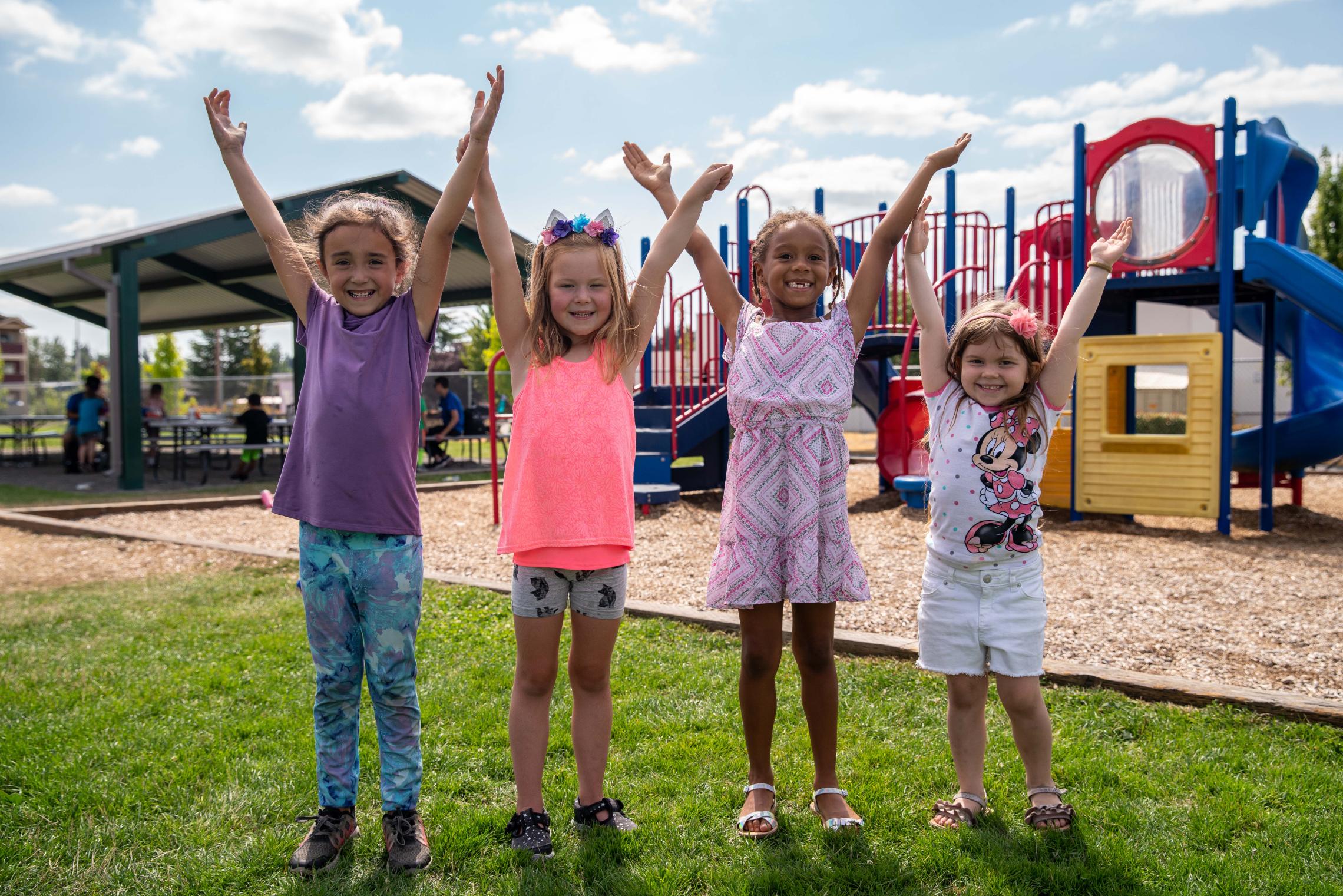 Day campers throw hands up in joy in front of the playground at the YMCA