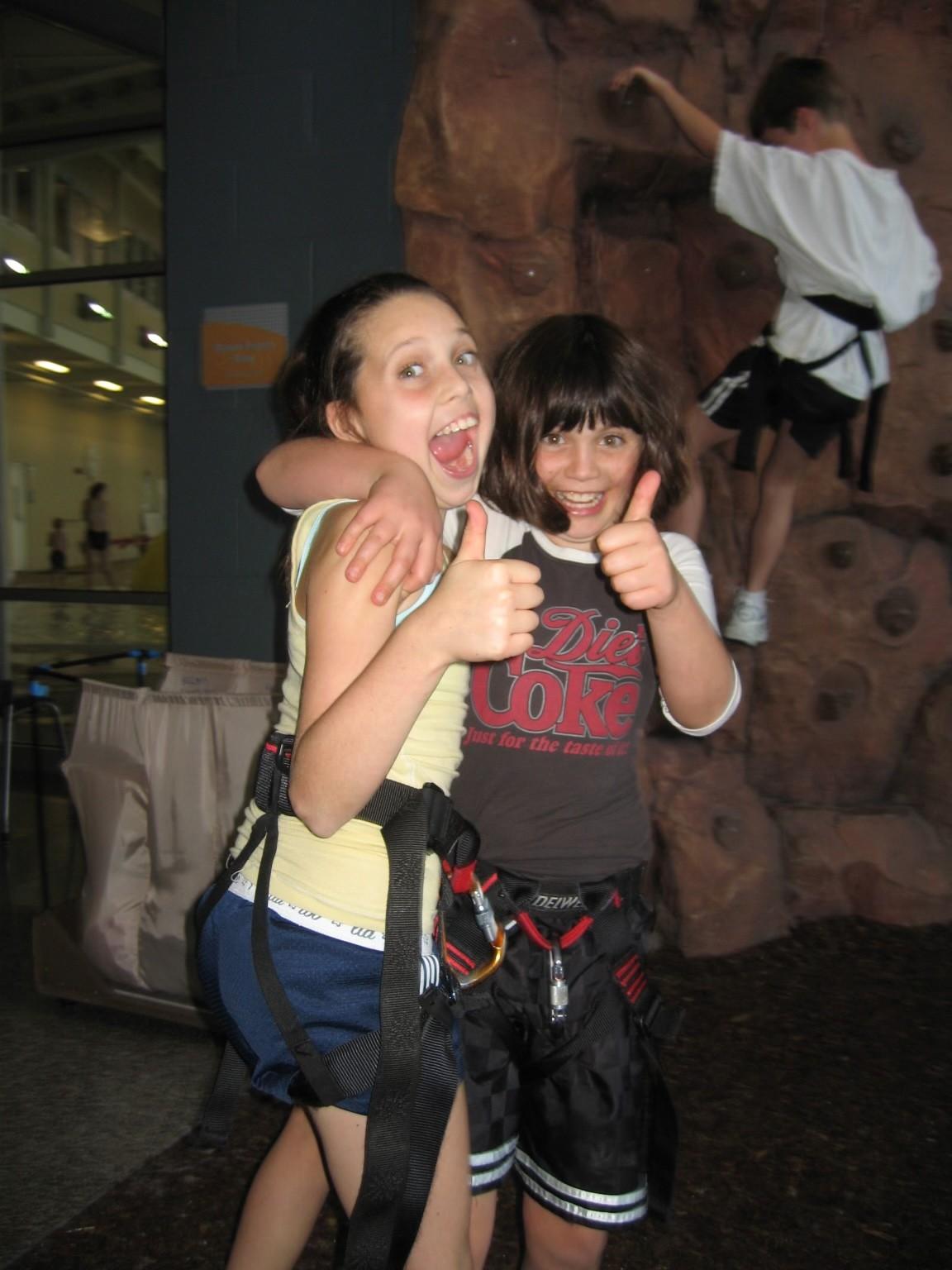 Photo of 2 rock climbing students giving a thumbs up in front of the rock wall at the YMCA