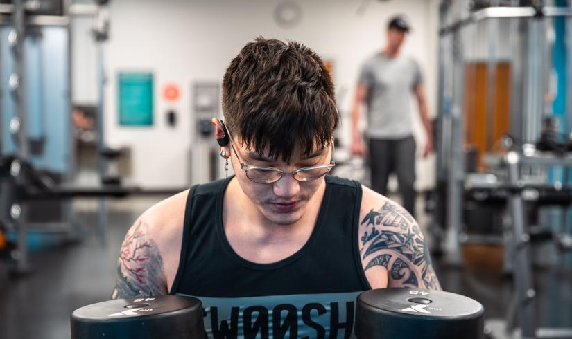 A young Asian American man reflects and holds two 45 pound free weights at the University YMCA Student Center.