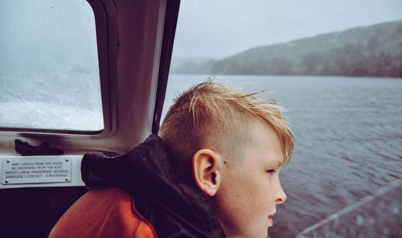 A young boy looks out over the water on a gray day. His eyes are off camera centered on what's beyond the frame.