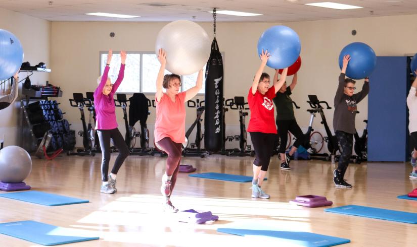 A group of active older adults holds yoga balls above their head as they work on movement and balance in a core yoga class. 