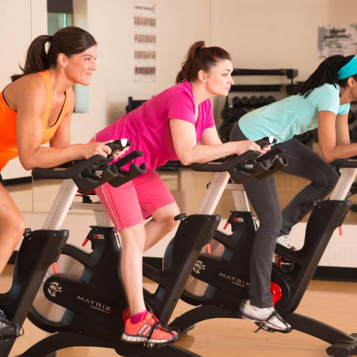 Three women on stationary bikes enjoy a group exercise class