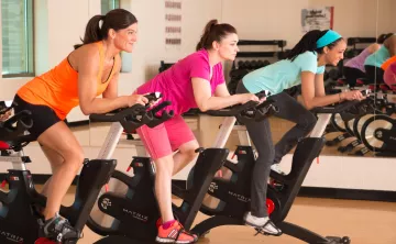 Three women on stationary bikes enjoy a group exercise class