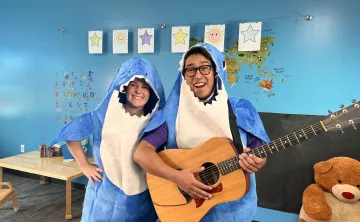 Instructors Lauren and Gabriel are in shark costumes and smiling as Gabriel holds an acoustic guitar.